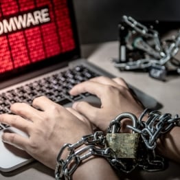 Hands chained with a padlock typing on a laptop showing a ransomware attack warning; symbolizing data encryption and cyber extortion.